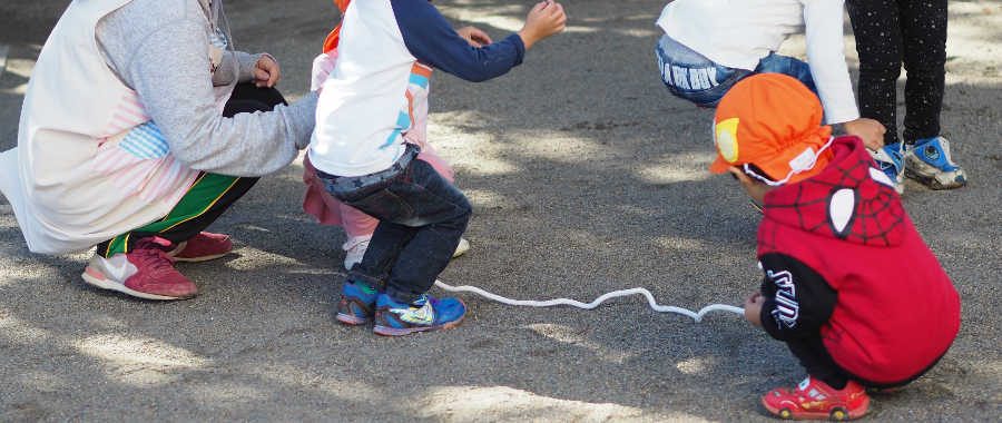 園庭で先生と縄あそびをする子どもたちの後ろ姿